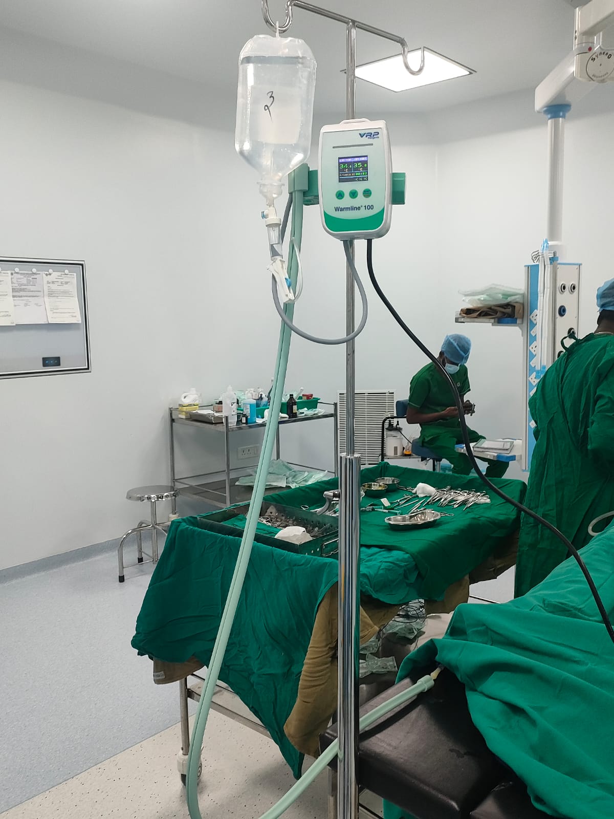Warmline 100 dry heat blood and fluid warmer device mounted on an IV pole in a hospital operating theater setup